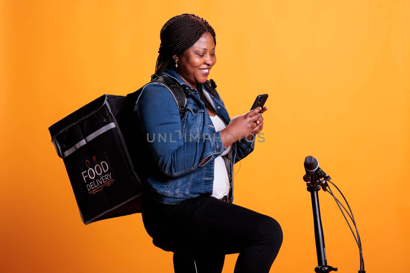 Restaurant courier standing on bicycle holding smartphone while checking client adreess on fast food app, carrying thermal backpack ready to deliver takeout lunch. Food service and transportation