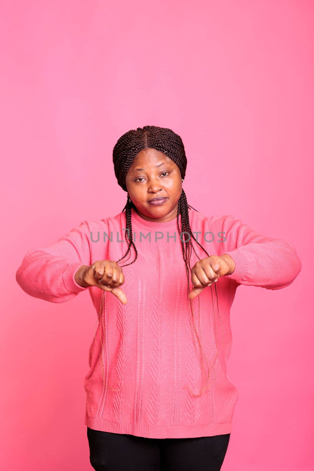 Displeased unhappy woman showing thumbs down gesture on camera in studio, gesturing failure sign with fingers. Dissatisfied person expressing disapproval and disappointment, doing dislike symbol.