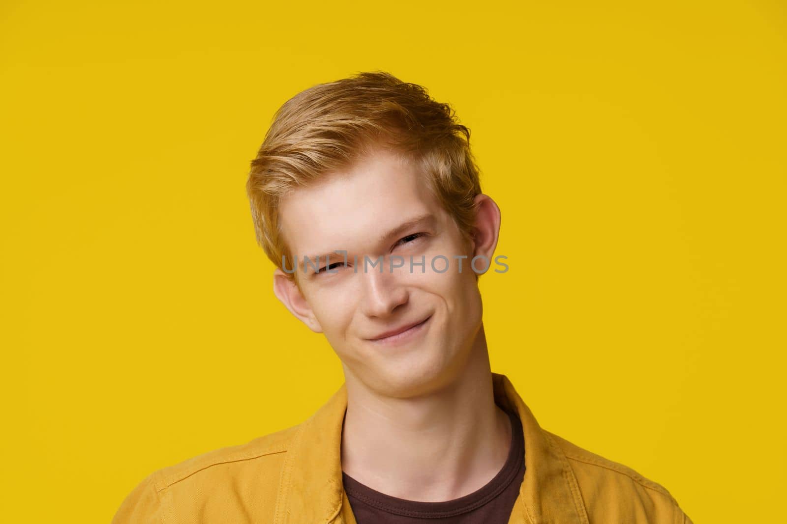 Emotion of Cunning and Deception Concept. A European Young Man shows an Emotion of Cunning and Distrust on a Yellow Background. High quality photo