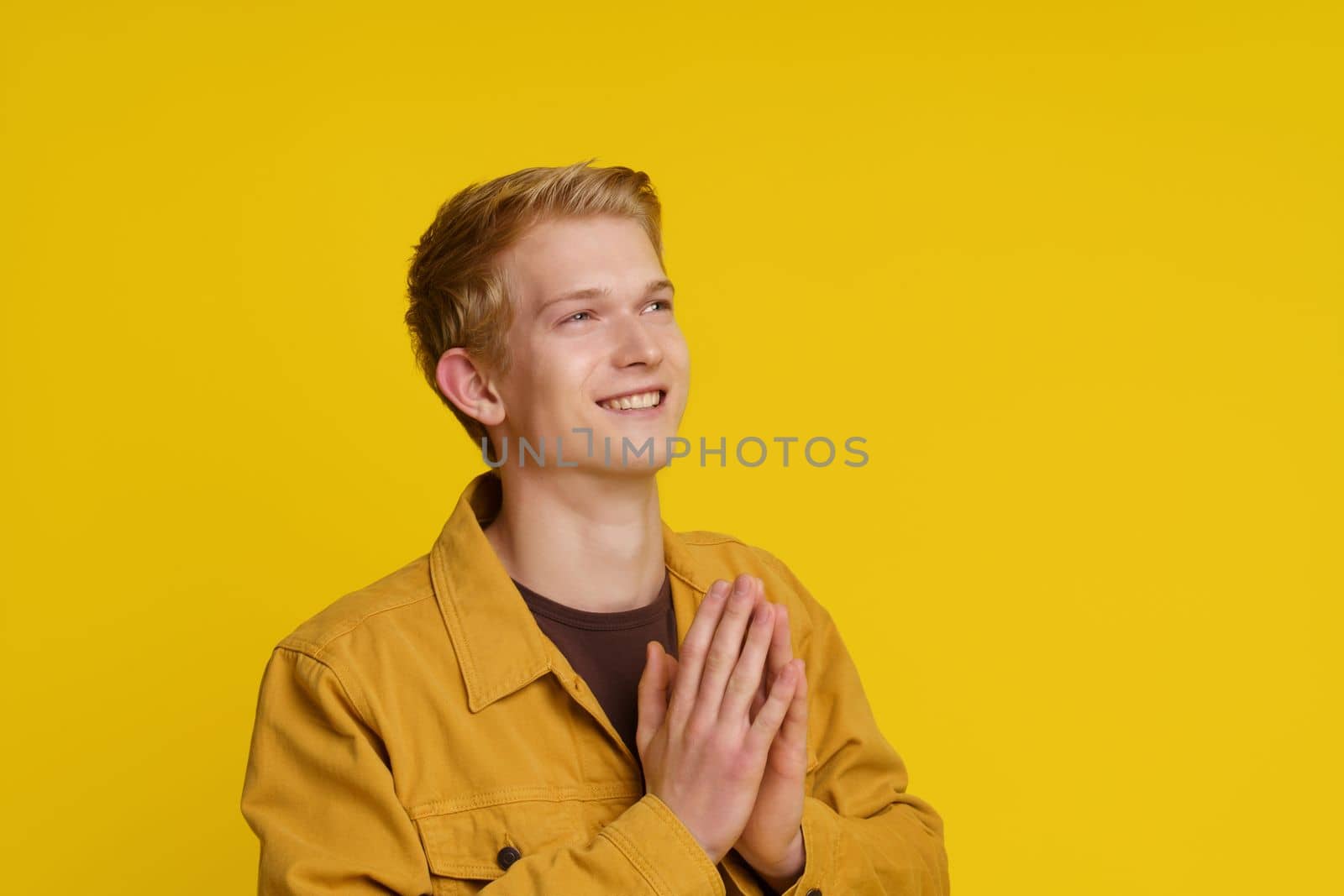 Happiness Gratitude Faith Concept. Smiling Young European Man Joined His Palms in a Gesture of Gratitude on a Yellow Background. High quality photo