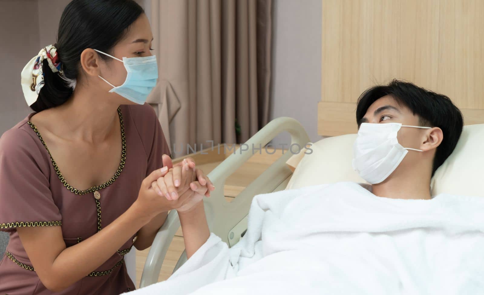 Young patient with attentive visitor and family holding hands in hospital sterile recovery room. The concept of family support for patients receiving hospital care. In-ward medical care and healthcare