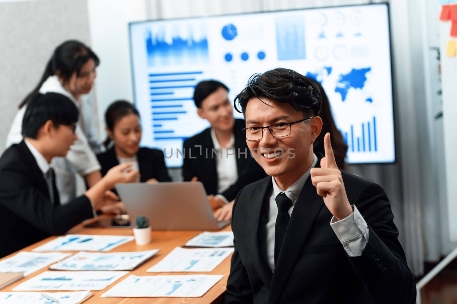 Focus portrait of successful confident male manager or executive in business wear with blurred background of businesspeople, colleagues working with financial report papers in office of harmony.