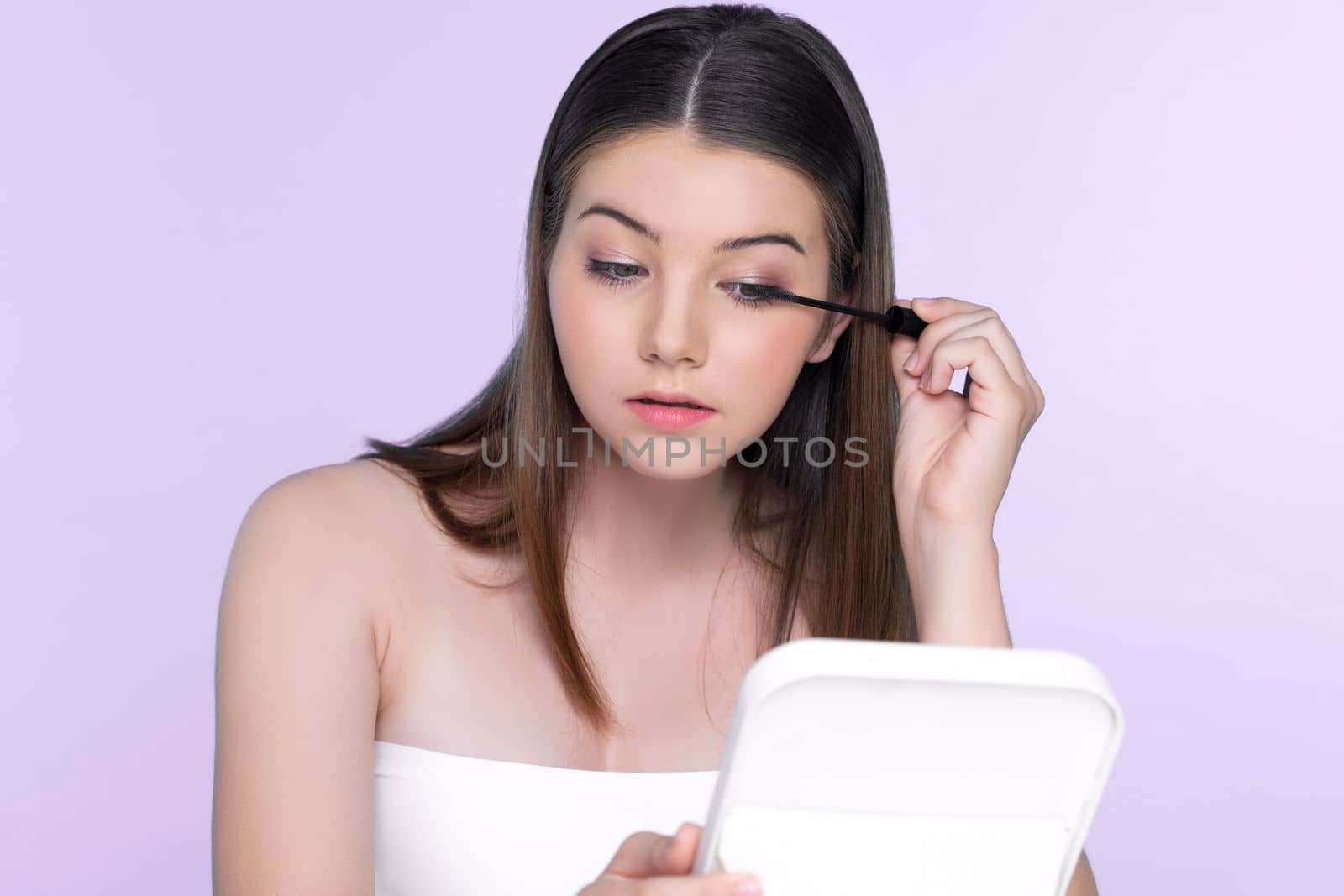 Closeup portrait of young charming applying makeup eyeshadow on her face with brush, mascara with flawless smooth skin for beauty concept.