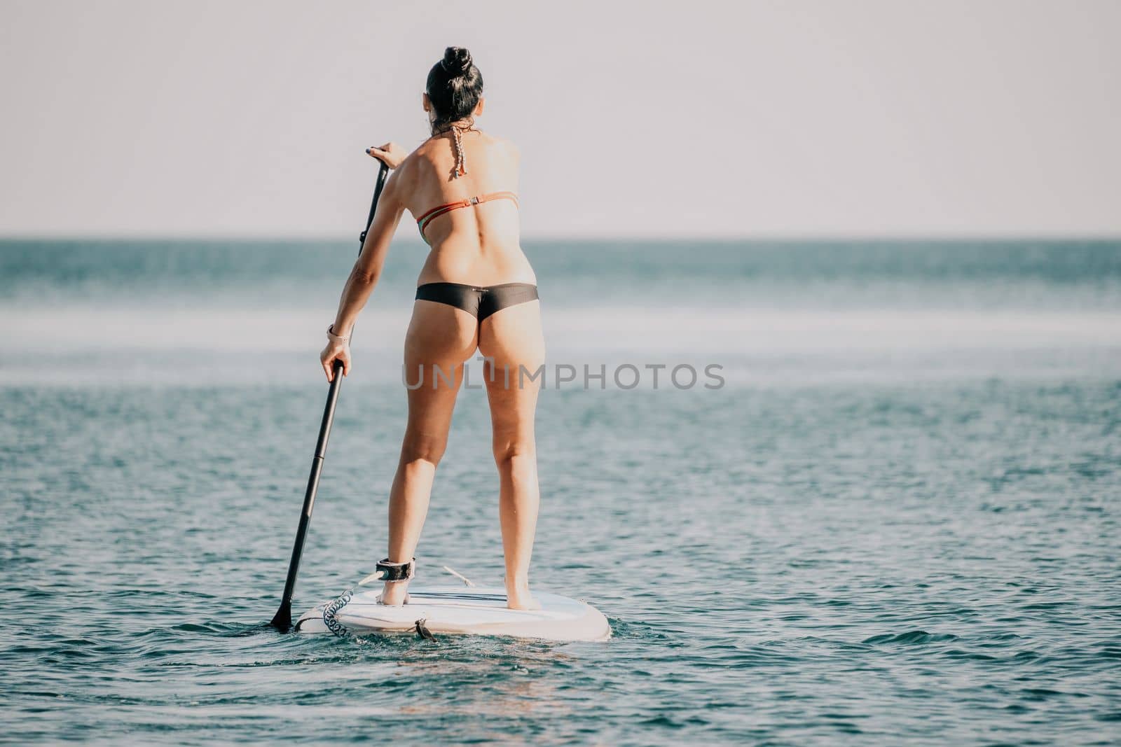 Sea woman sup. Silhouette of happy middle aged woman in rainbow bikini, surfing on SUP board, confident paddling through water surface. Idyllic sunset. Active lifestyle at sea or river