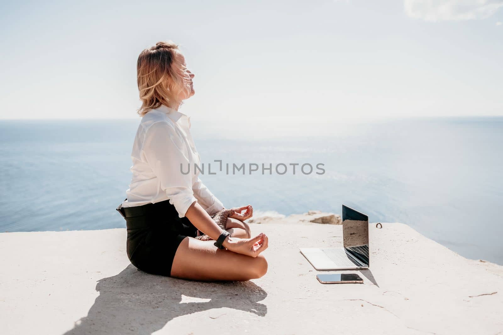 Happy girl doing yoga with laptop working at the beach. beautiful and calm business woman sitting with a laptop in a summer cafe in the lotus position meditating and relaxing. freelance girl remote work beach paradise