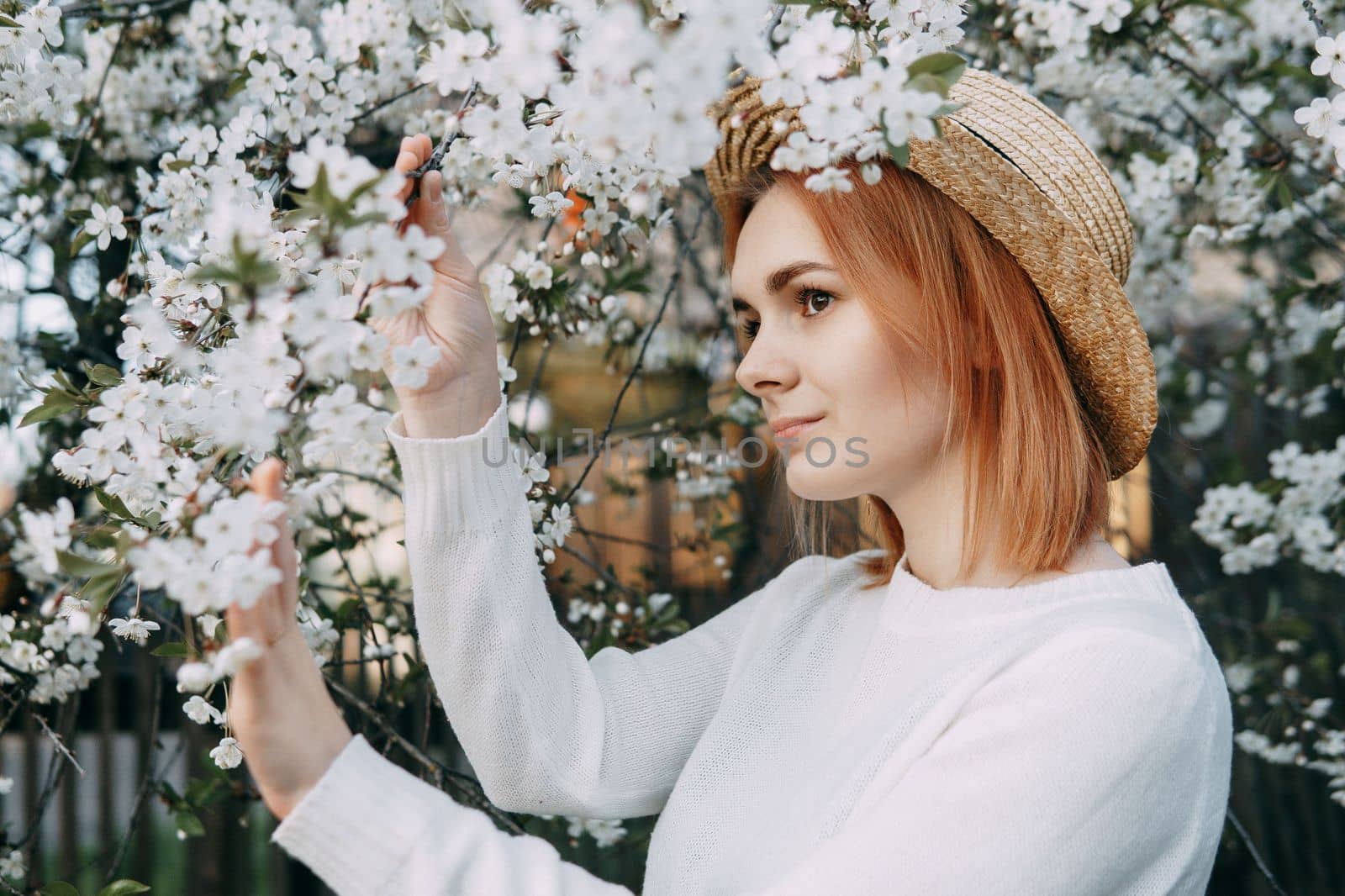 Portrait of a woman in a straw hat in a cherry blossom. Free outdoor recreation, spring blooming garden