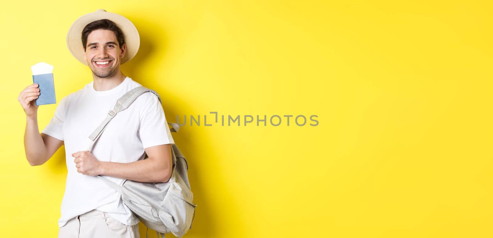 Tourism and vacation. Smiling young guy going on trip, holding backpack and showing passport with tickets, standing over yellow background by Benzoix