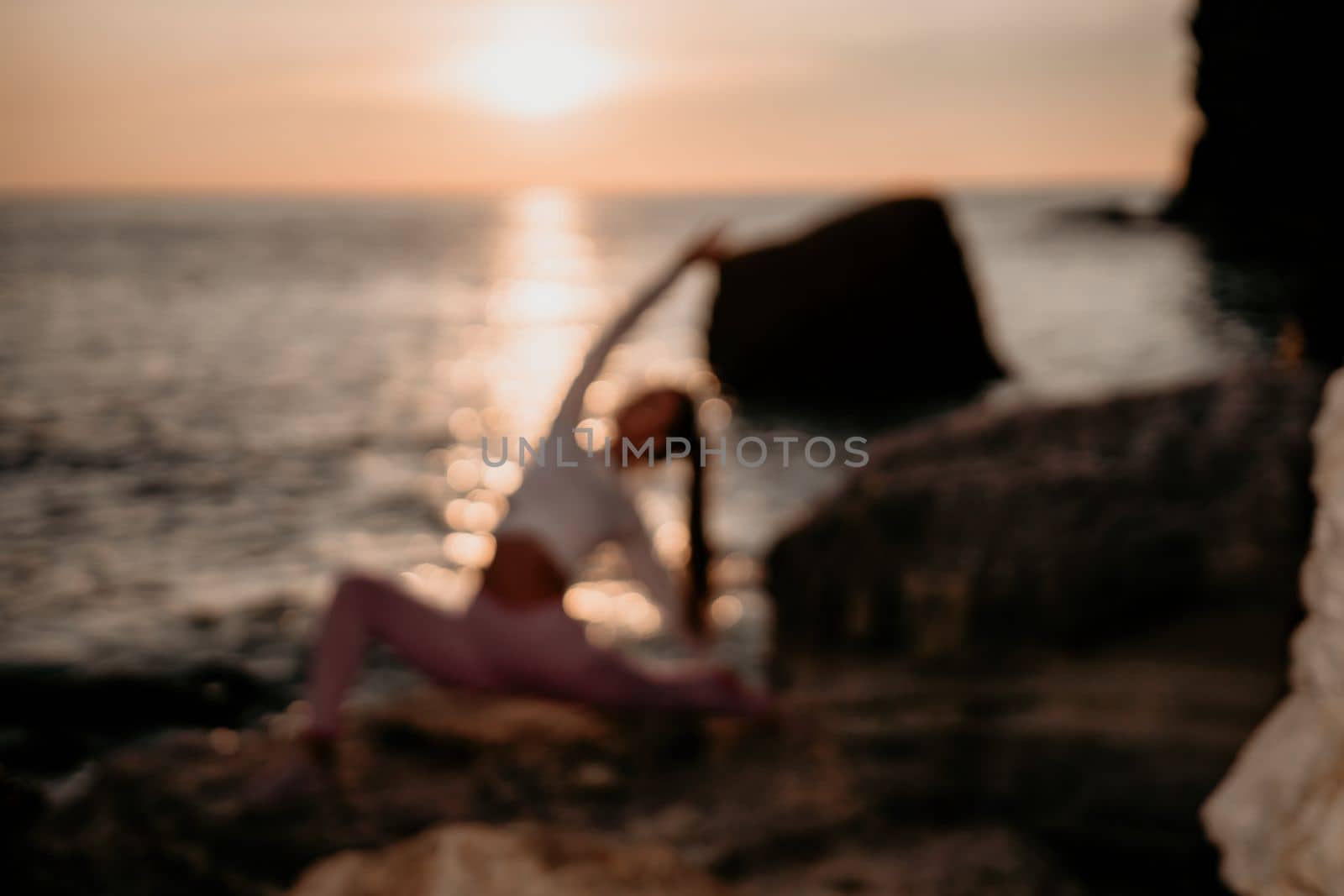 Young woman with black hair, fitness instructor in pink sports leggings and tops, doing pilates on yoga mat with magic pilates ring by the sea on the beach. Female fitness daily yoga concept