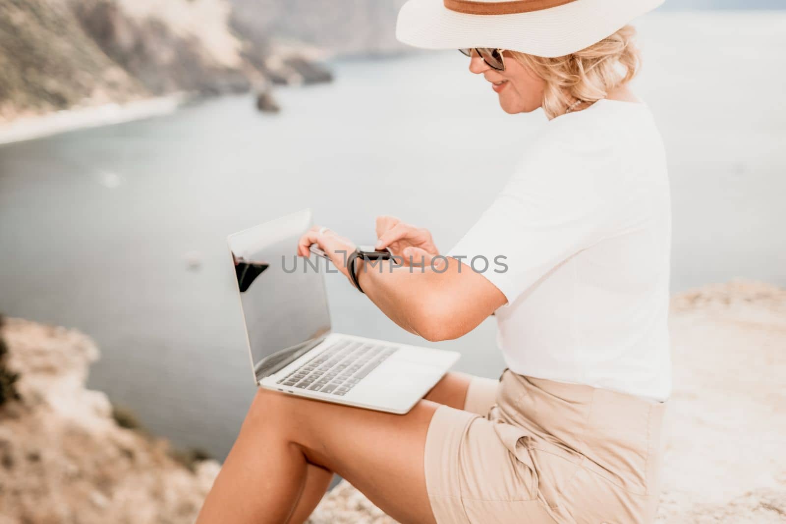 Digital nomad, Business woman working on laptop by the sea. Pretty lady typing on computer by the sea at sunset, makes a business transaction online from a distance. Freelance, remote work on vacation by panophotograph