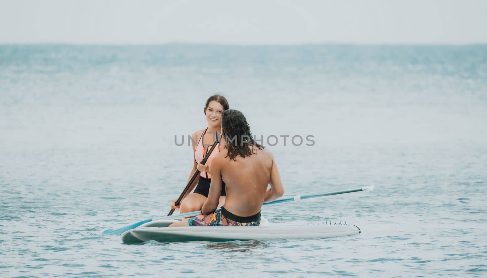 Sea woman and man on sup. Silhouette of happy young woman and man, surfing on SUP board, confident paddling through water surface. Idyllic sunset. Active lifestyle at sea or river. by panophotograph