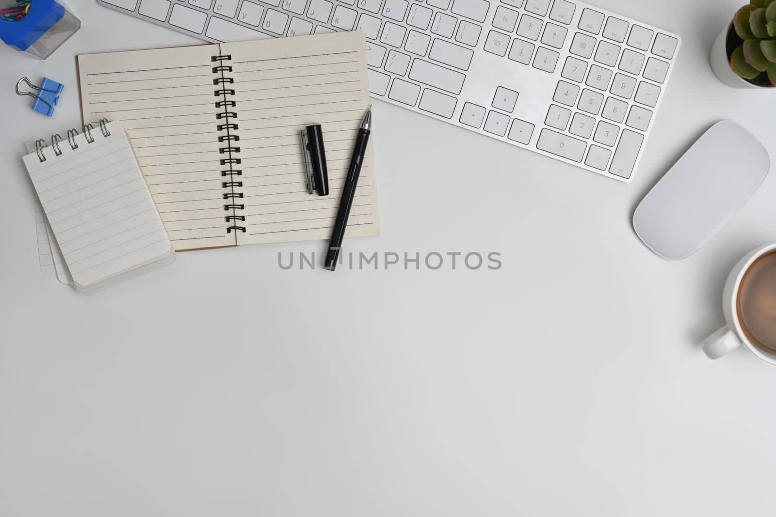 Top view of blank notepad, cup of coffee, wireless headphone and mouse on white table. Copy space for your text by prathanchorruangsak