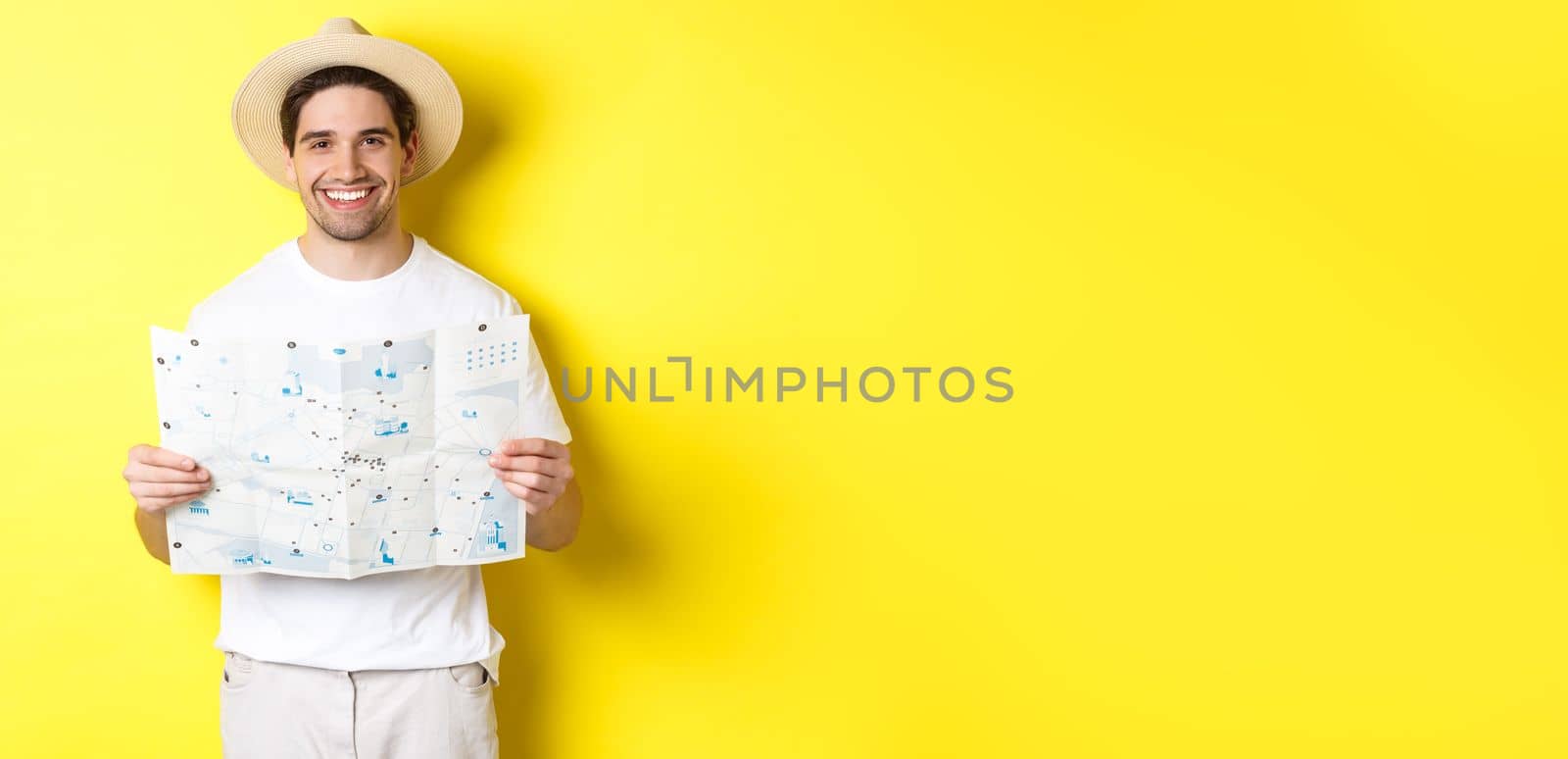 Travelling, vacation and tourism concept. Smiling young man going on trip, holding road map and smiling, standing over yellow background.