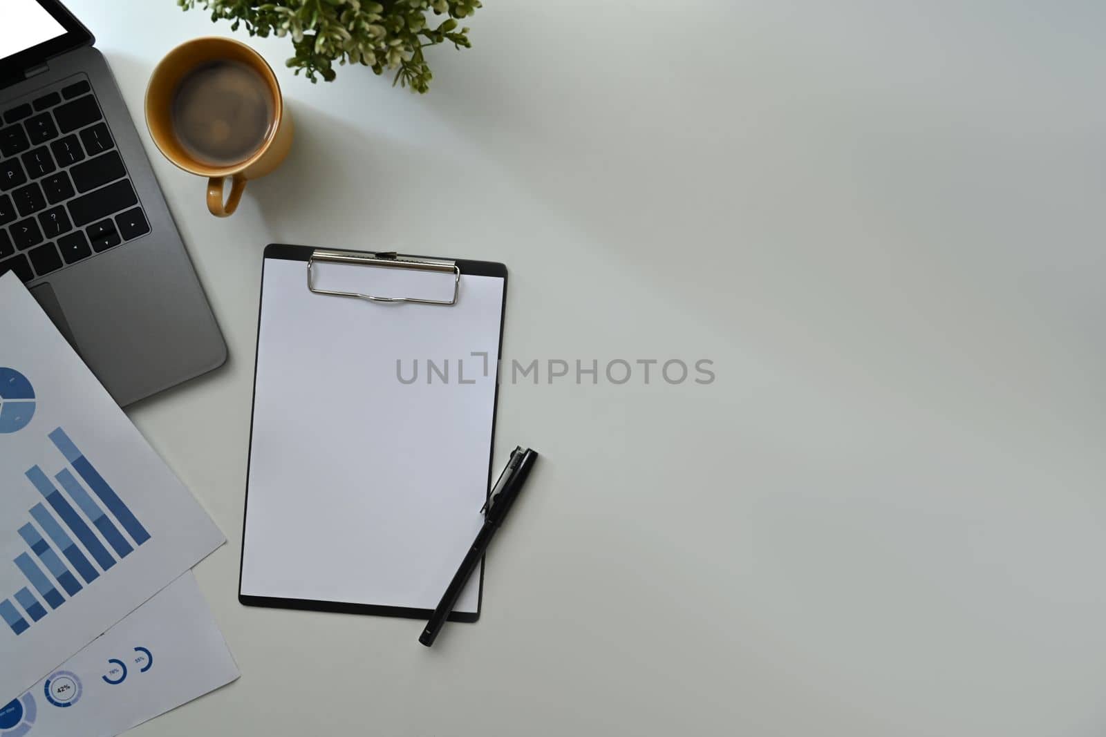 Blank clipboard, laptop computer, coffee cup and financial reports on white office by prathanchorruangsak