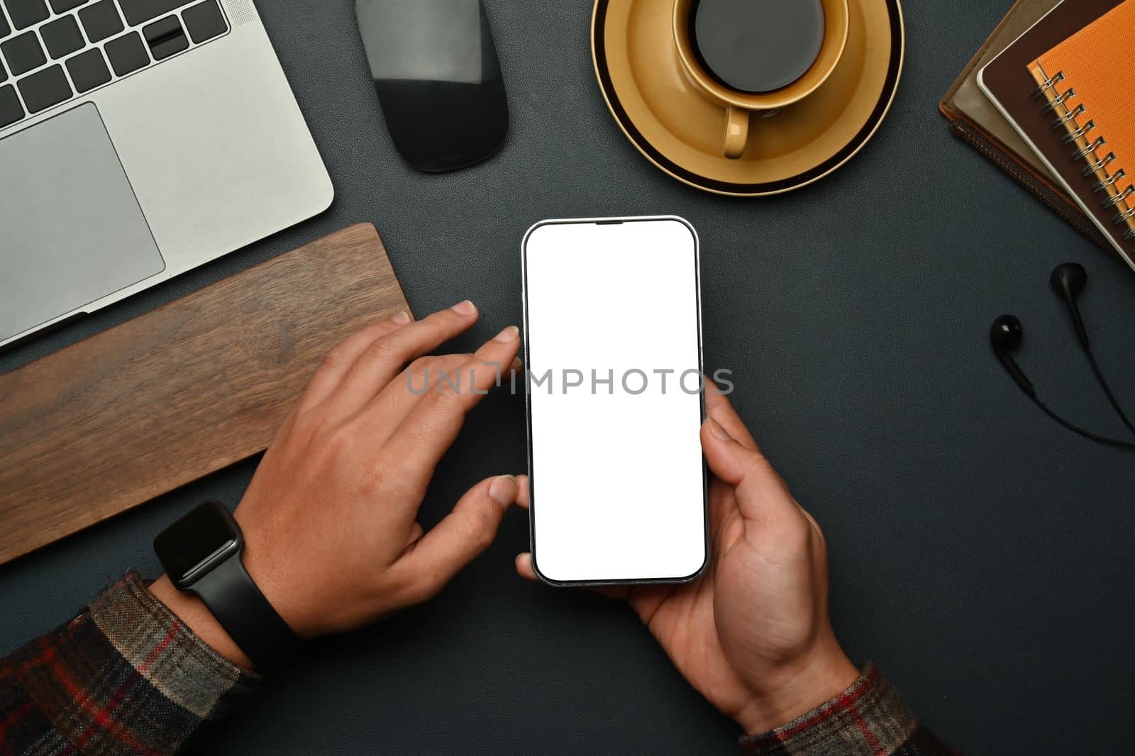 Overhead view of hipster man hands holding smart phone while sitting front of laptop at workstation by prathanchorruangsak