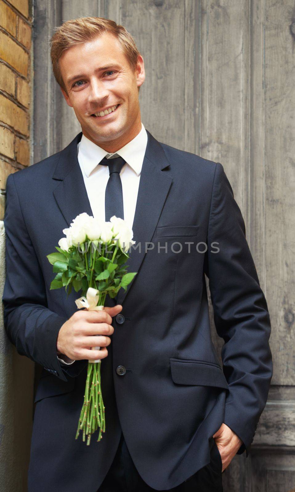 Rose, portrait and man with gift for valentines day, anniversary or first date while waiting on door background. Face, flowers and gentleman with sweet, gesture or offering for love and romance.