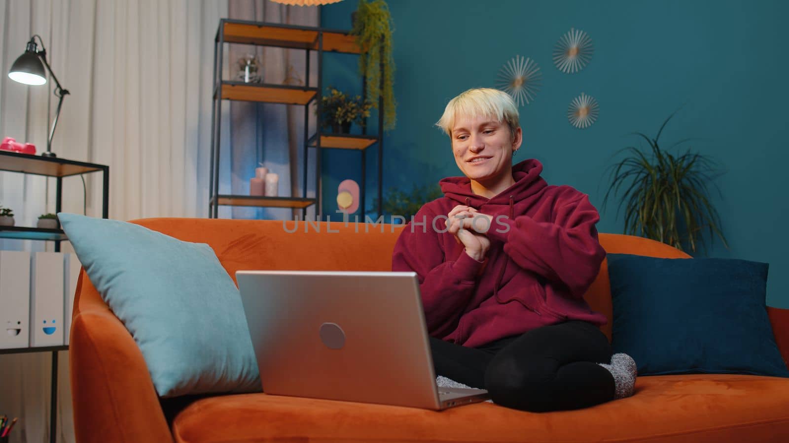 Young woman with short hair sitting on couch looking at camera, making video webcam conference call with friends or family, enjoying pleasant conversation. Girl laughing waving hello at night home