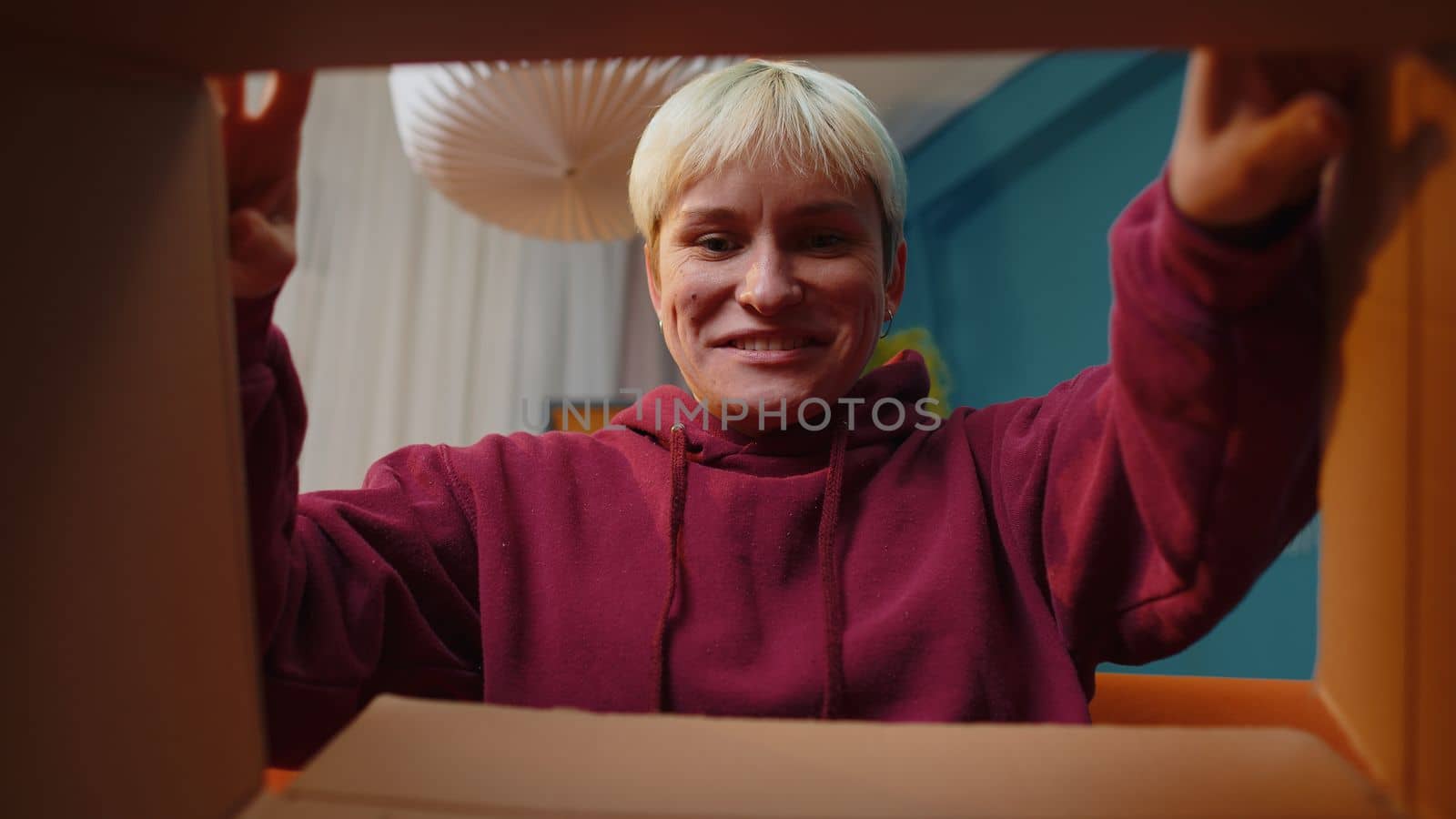 Happy surprised winner woman unpacking delivery parcel at home. Smiling satisfied girl shopper online shop customer opening cardboard box receiving purchase gift headphones by fast postal shipping