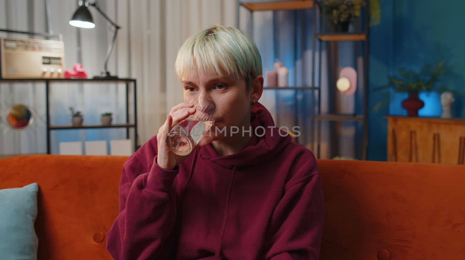 Thirsty woman with short blonde hair holding glass of natural aqua make sips drinking still water preventing dehydration at home. Girl with good life habits, healthy slimming, weight loss concept