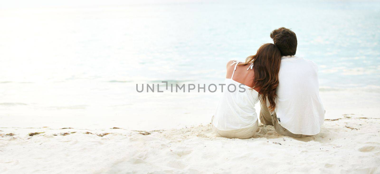 Bonding intimately upon the beach - Love Romance. Two young lovers looking over a calm ocean towards a beautiful sunset - Copyspace