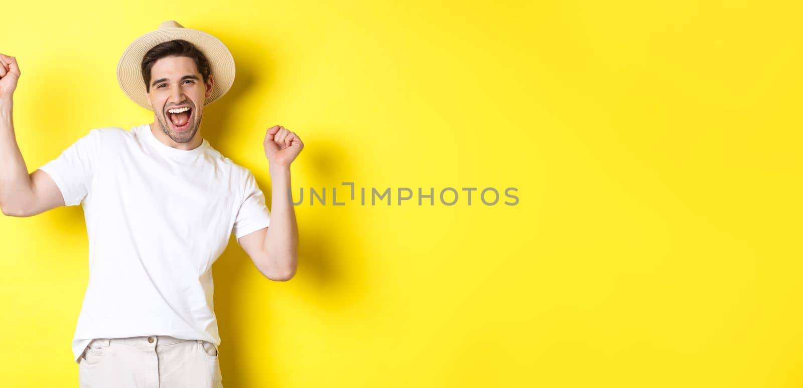 Concept of tourism and lifestyle. Happy man tourist celebrating, rejoicing over vacation, standing over yellow background.