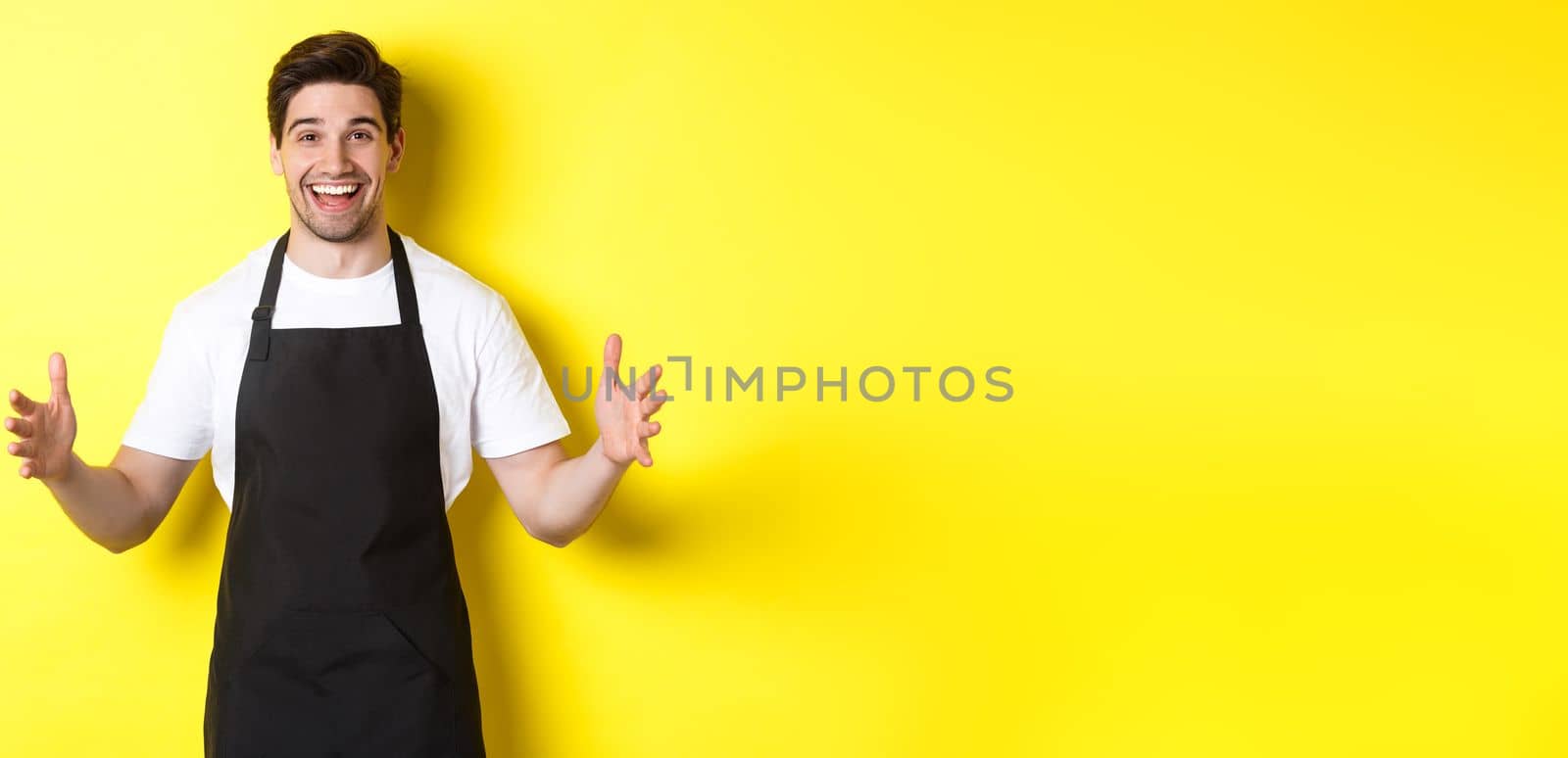 Happy barista holding something big, shaping large object, standing over yellow background.