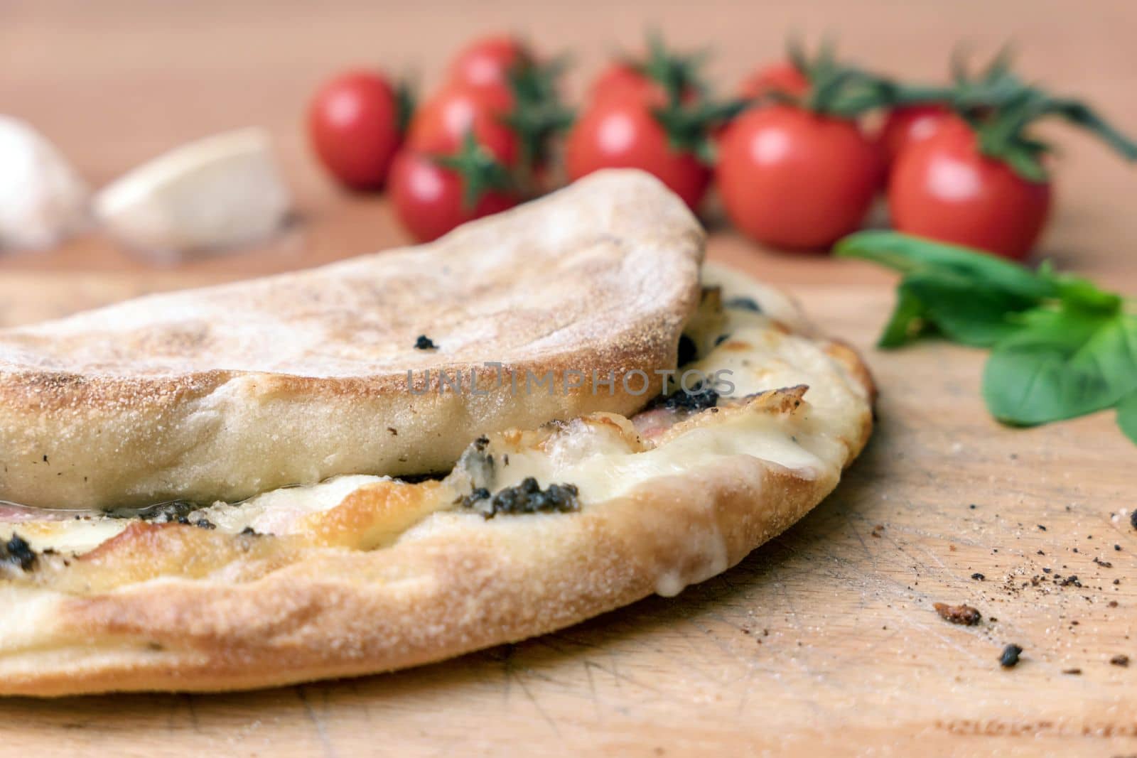 Italian food, closed calzone pizza on rustic wooden background. On blurred background small red tomatoes.
Selective focus