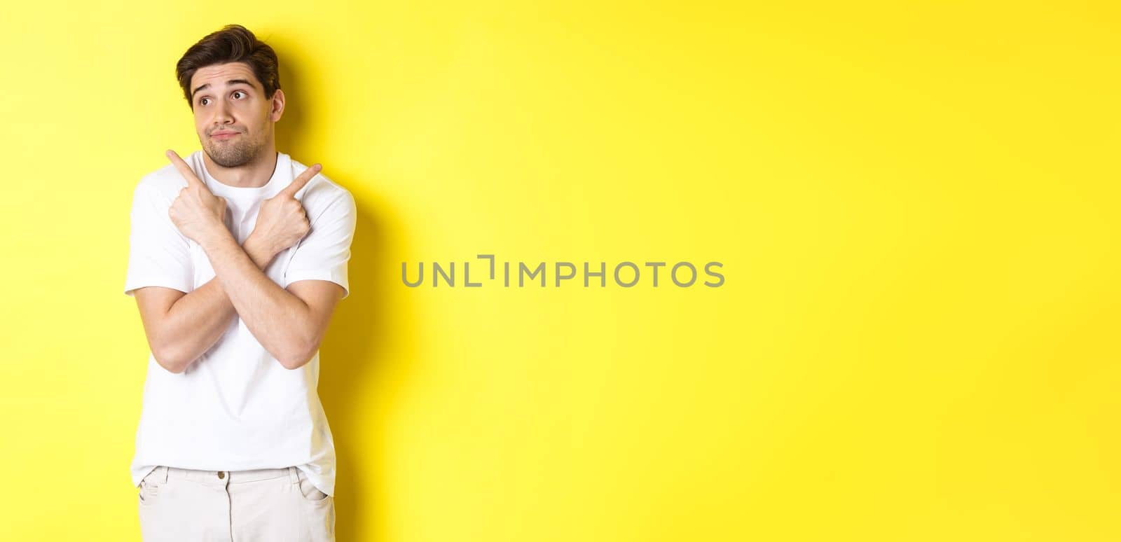 Indecisive man shrugging, pointing fingers sideways, troubled to choose, standing over yellow background by Benzoix