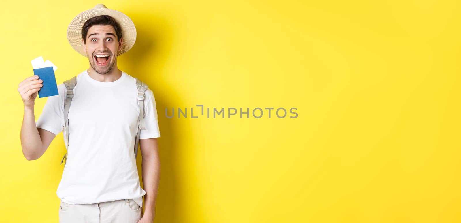 Tourism and vacation. Happy man tourist showing his passport with tickets, going on journey, standing over yellow background with backpack by Benzoix