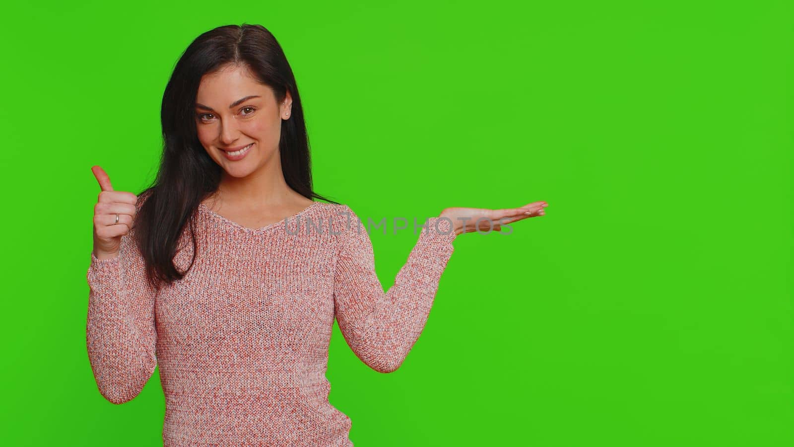 Lovely woman showing thumbs up and pointing empty place, advertising area for commercial text, copy space for goods promotion discount. Young pretty girl. Indoor studio shot on red wall background