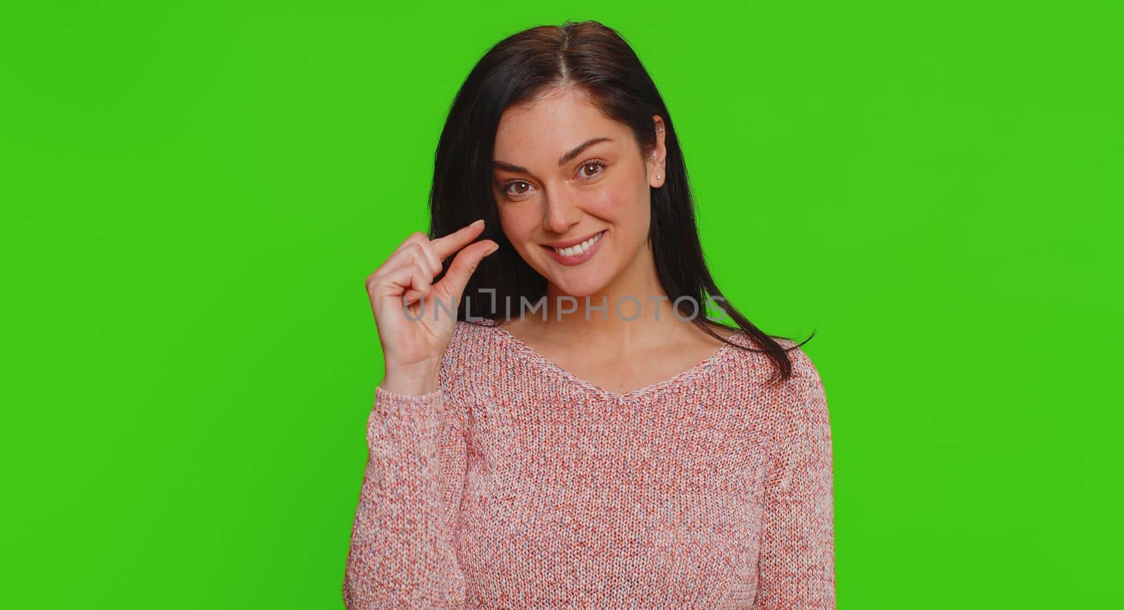 Need some more, please give me. Lovely woman showing a little bit gesture with sceptic smile, showing minimum sign, measuring small size. Young adult girl isolated alone on green chroma key background