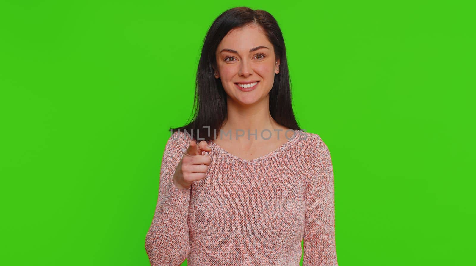 Hey you. I choose you. Young woman in sweater smiling excitedly and pointing finger to camera, choosing lucky winner, indicating to awesome you. Pretty girl indoors isolated on chroma key background