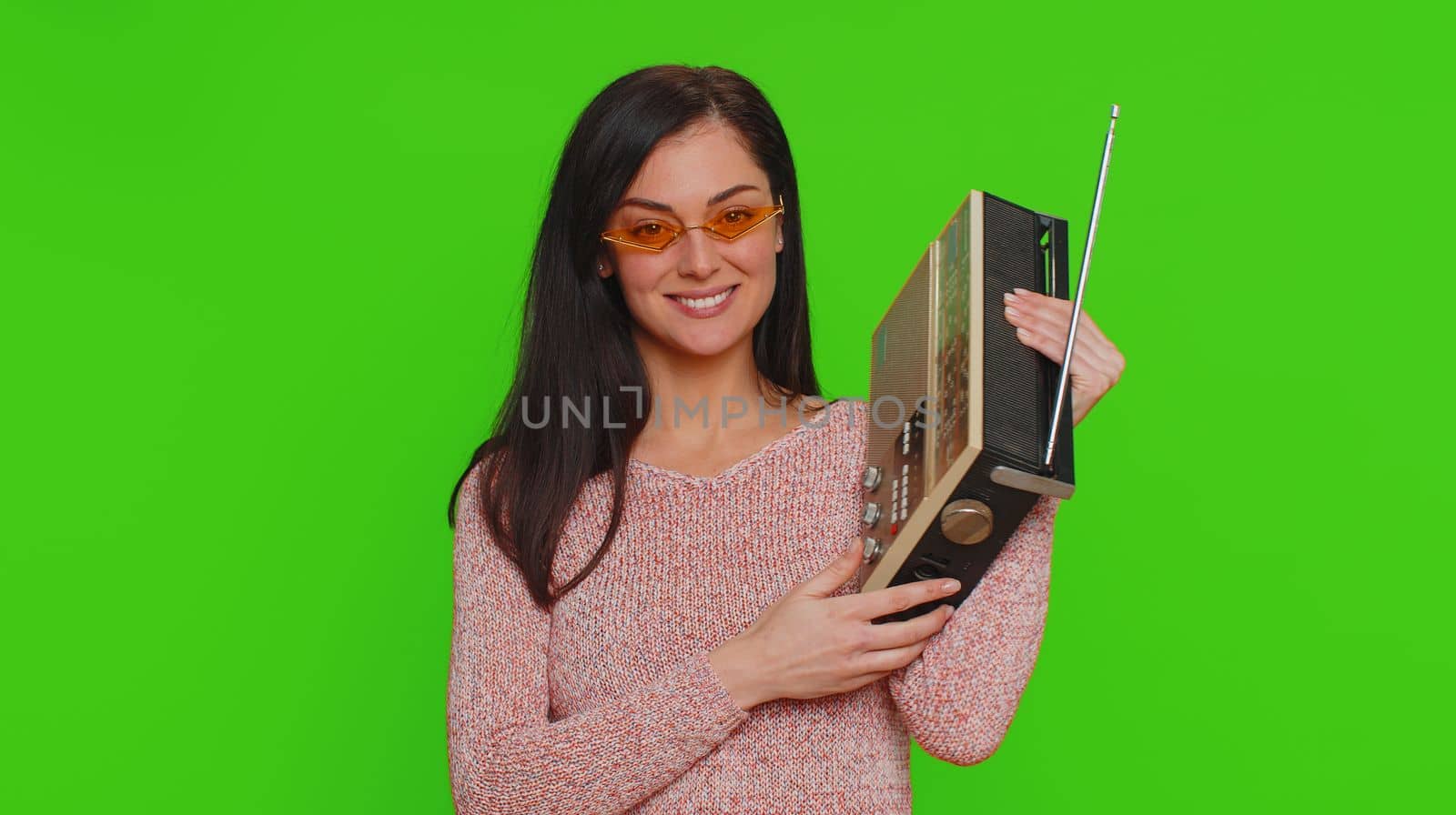 Lovely woman using retro tape record player to listen music, disco dancing of favorite track, having fun, entertaining, fan of vintage technologies. Young adult girl isolated on red wall background