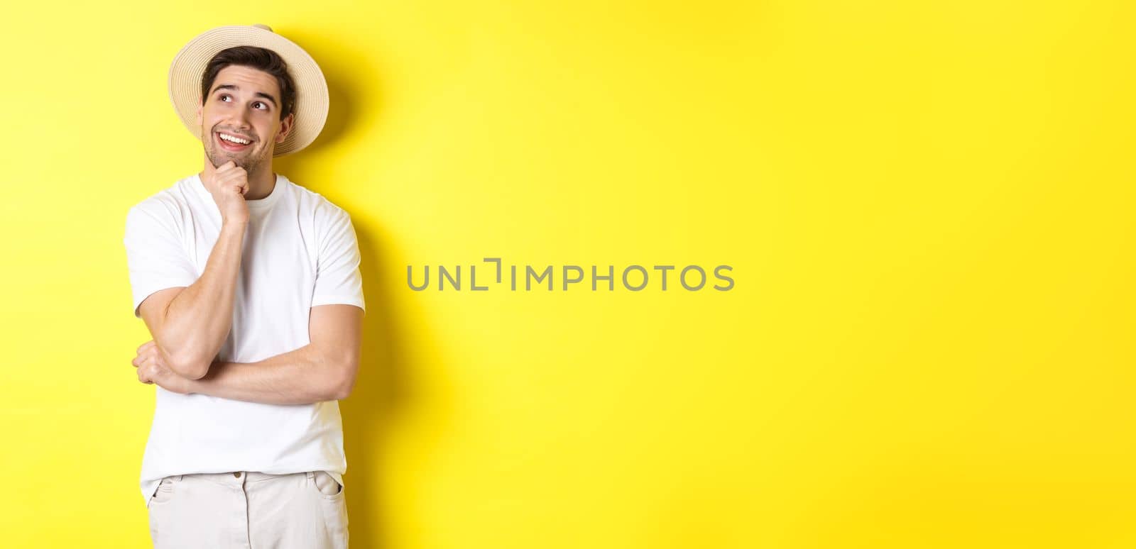 Young thoughtful man tourist imaging something, looking at upper left corner and smiling, thinking and standing over yellow background.