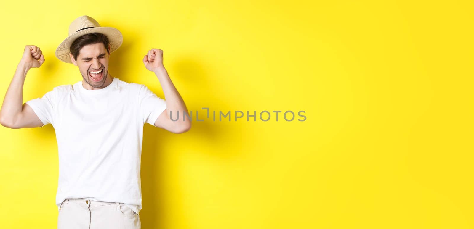 Concept of tourism and vacation. Happy man rejoicing, winning something or achieve goal, triumphing against yellow background by Benzoix