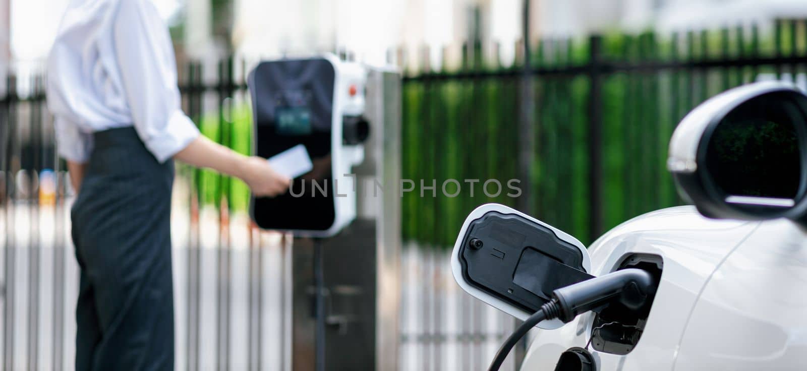 Focus progressive EV recharge with blurred woman using credit card in background by biancoblue