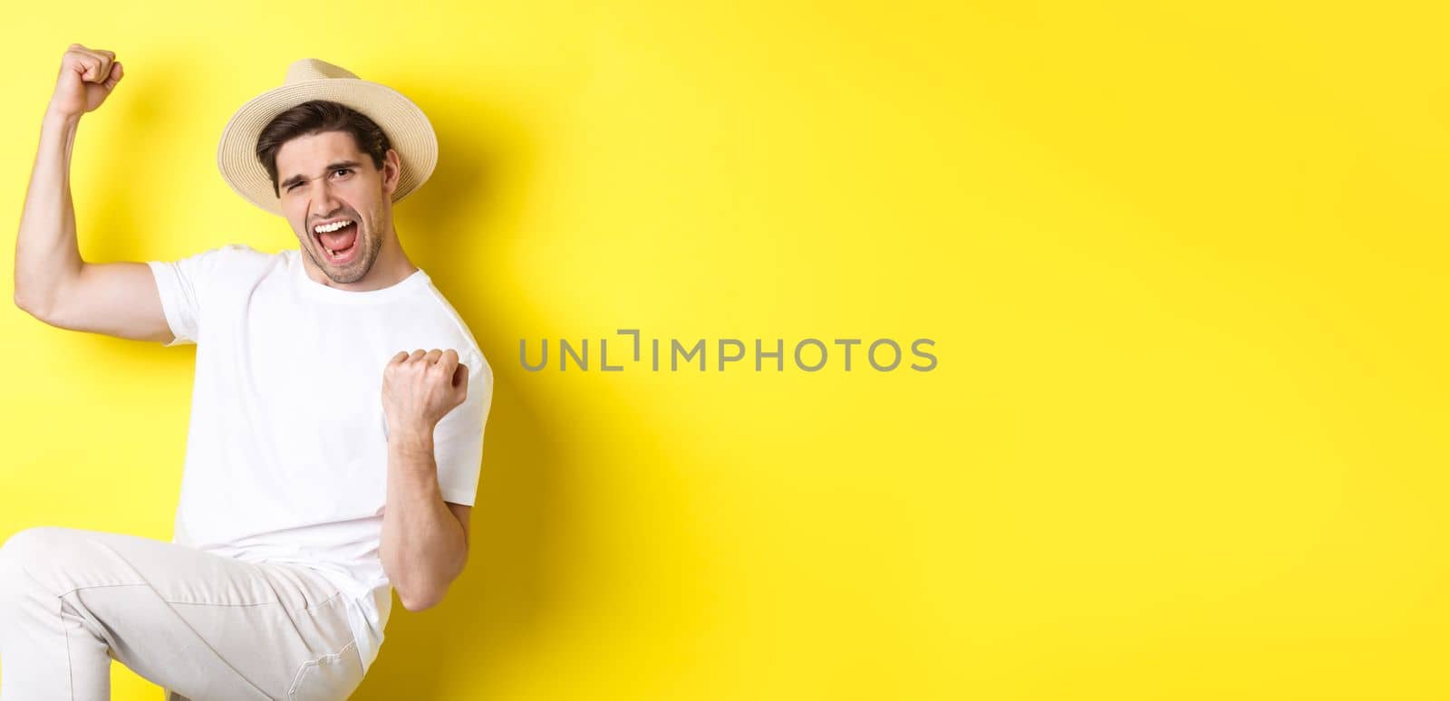 Concept of tourism and vacation. Lucky male tourist winning trip, rejoicing and saying yes, making fist pump while triumphing, standing against yellow background.