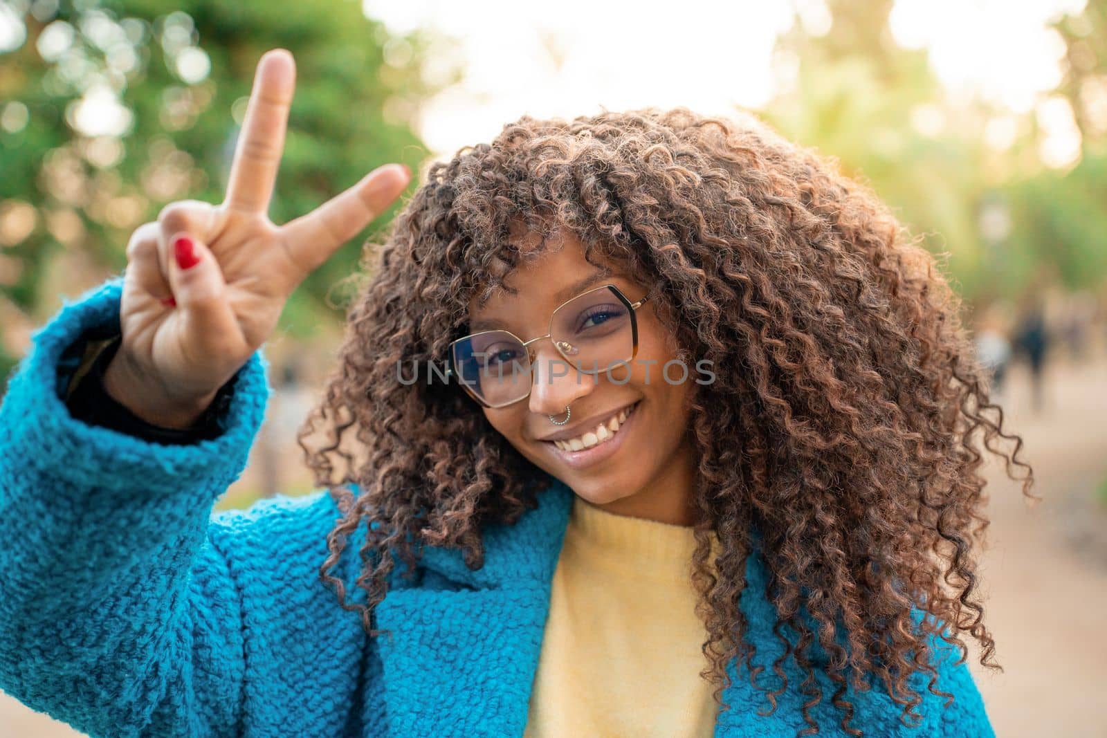 Portrait of a beautiful African American woman smile with beautiful Afro curly hair and glasses. Positive cheerful black female does the victory symbol with the fingers.
