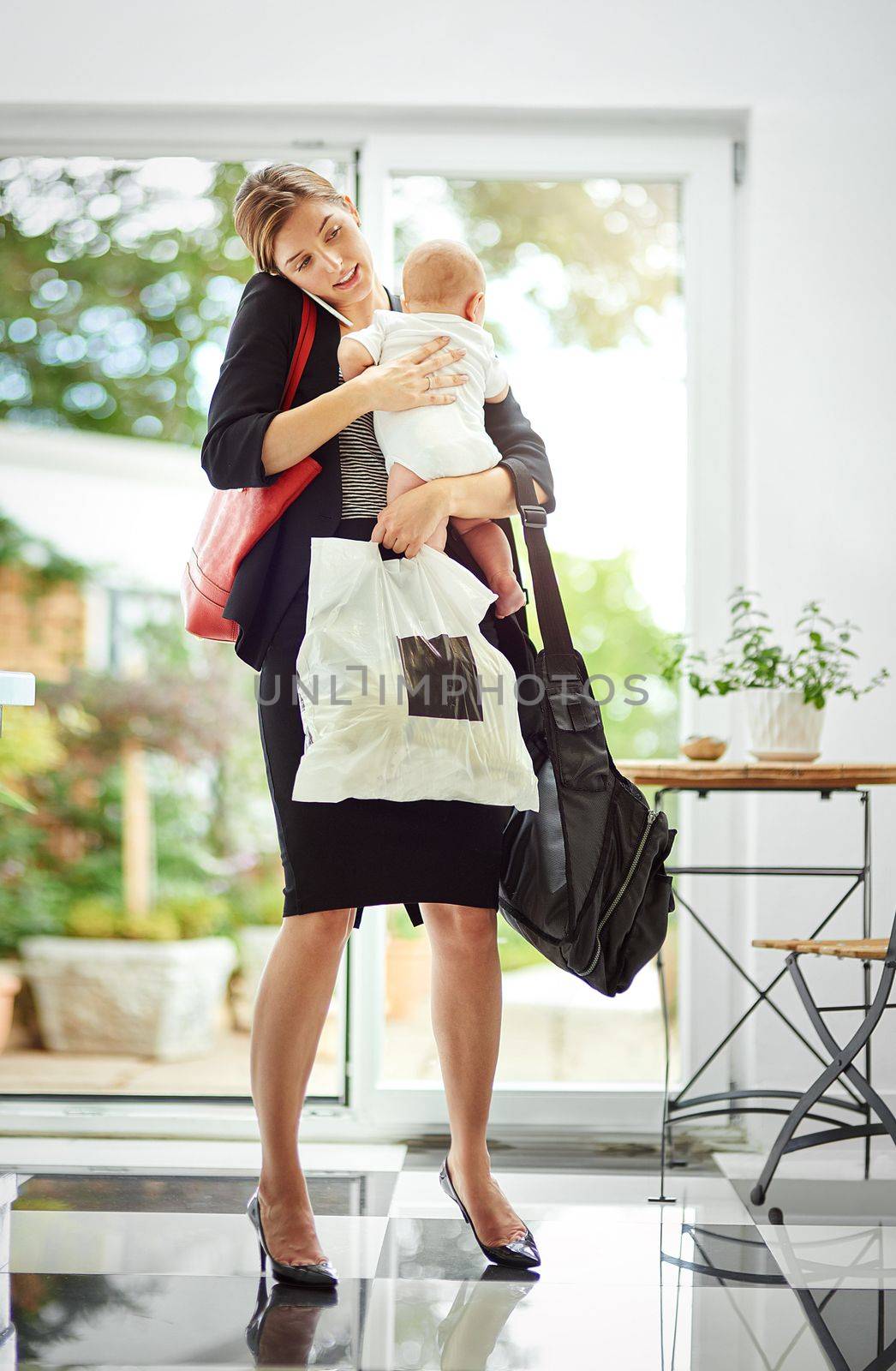Its hard being a working mom. a busy businesswoman carrying a shopping bag and her baby while talking on the phone on her return from work