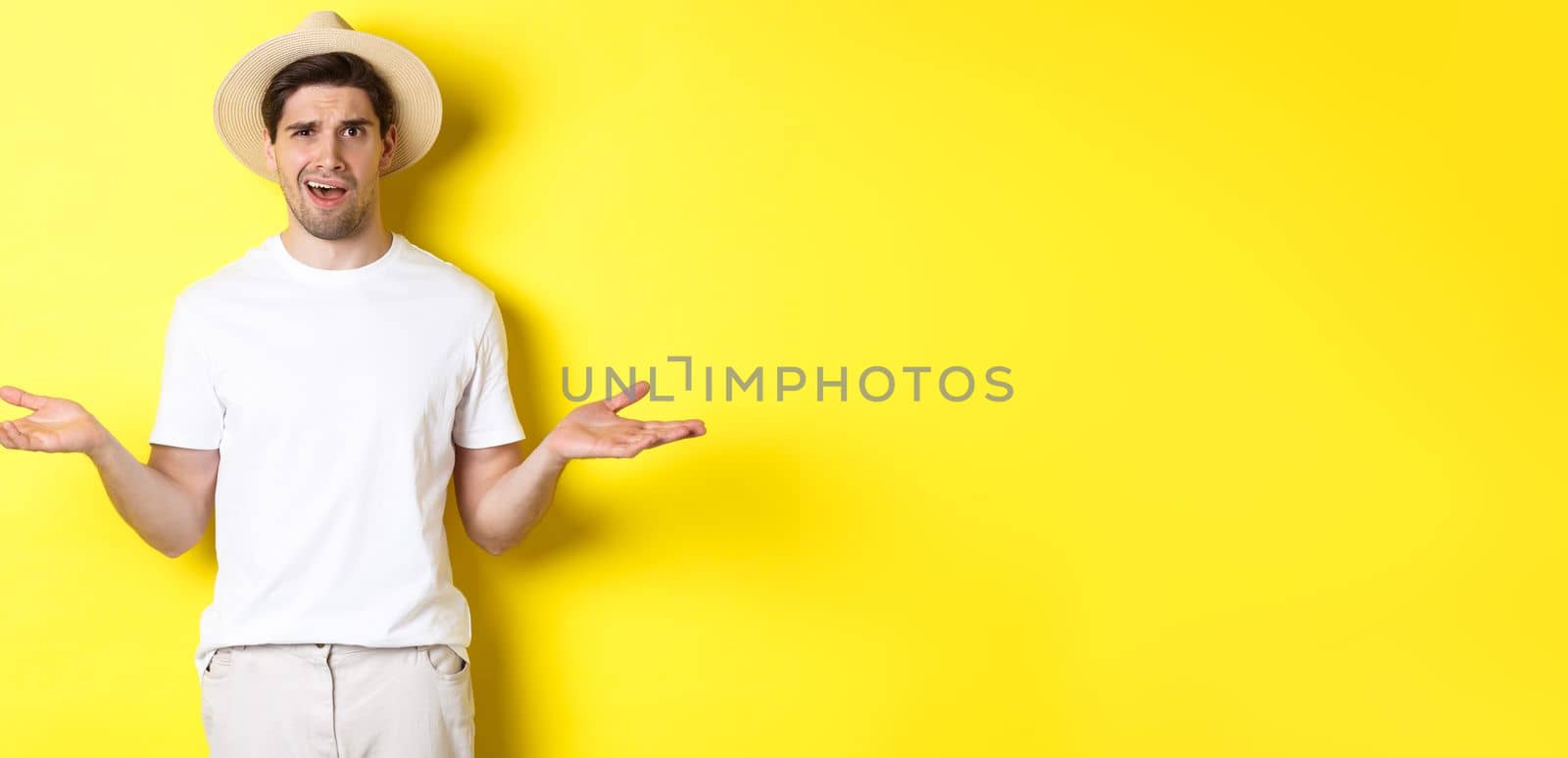 Concept of tourism and summer. Confused guy traveller shrugging, cant understand something, standing against yellow background.