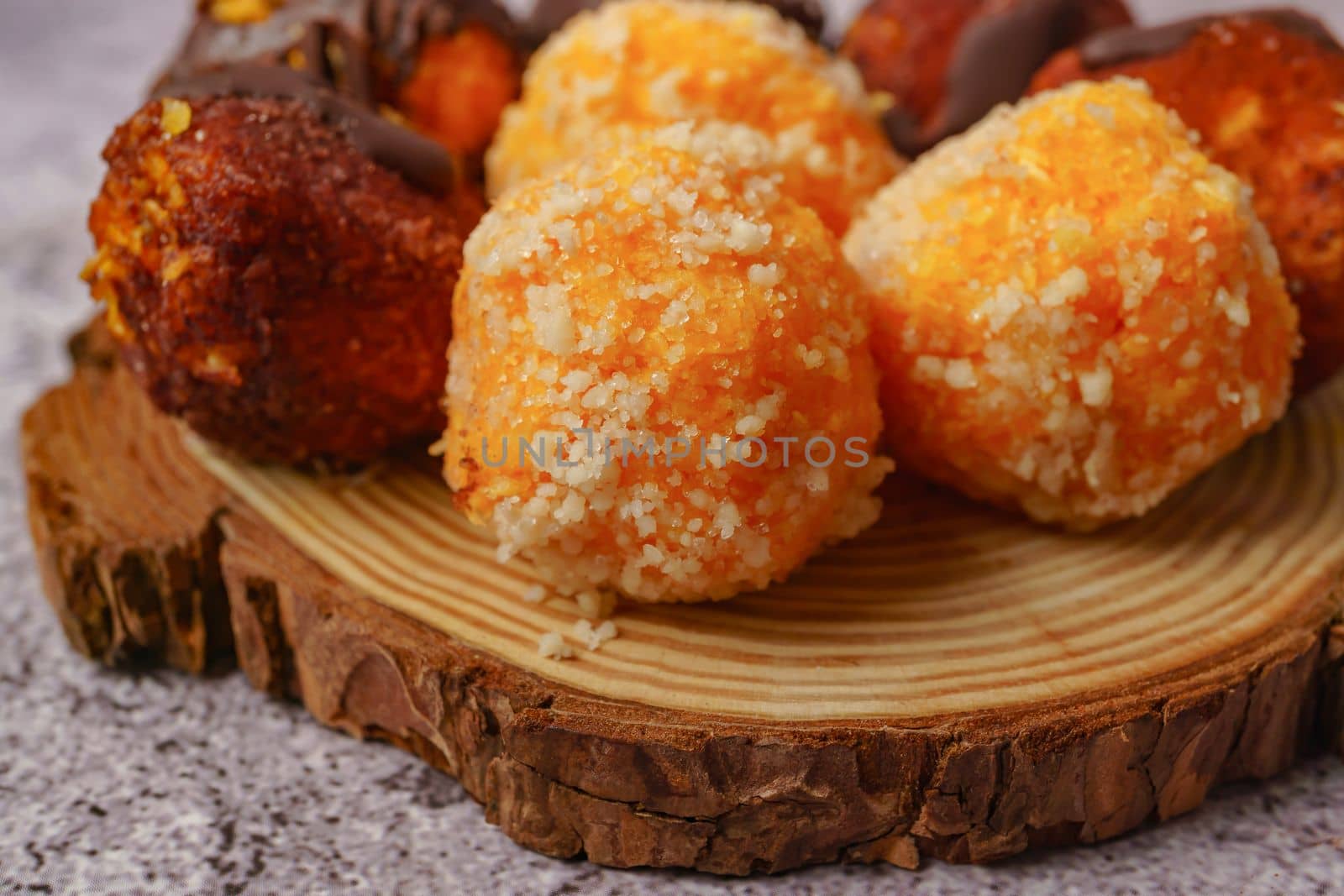 close-up of sweet truffles of different flavors on a wooden disk on a gray background