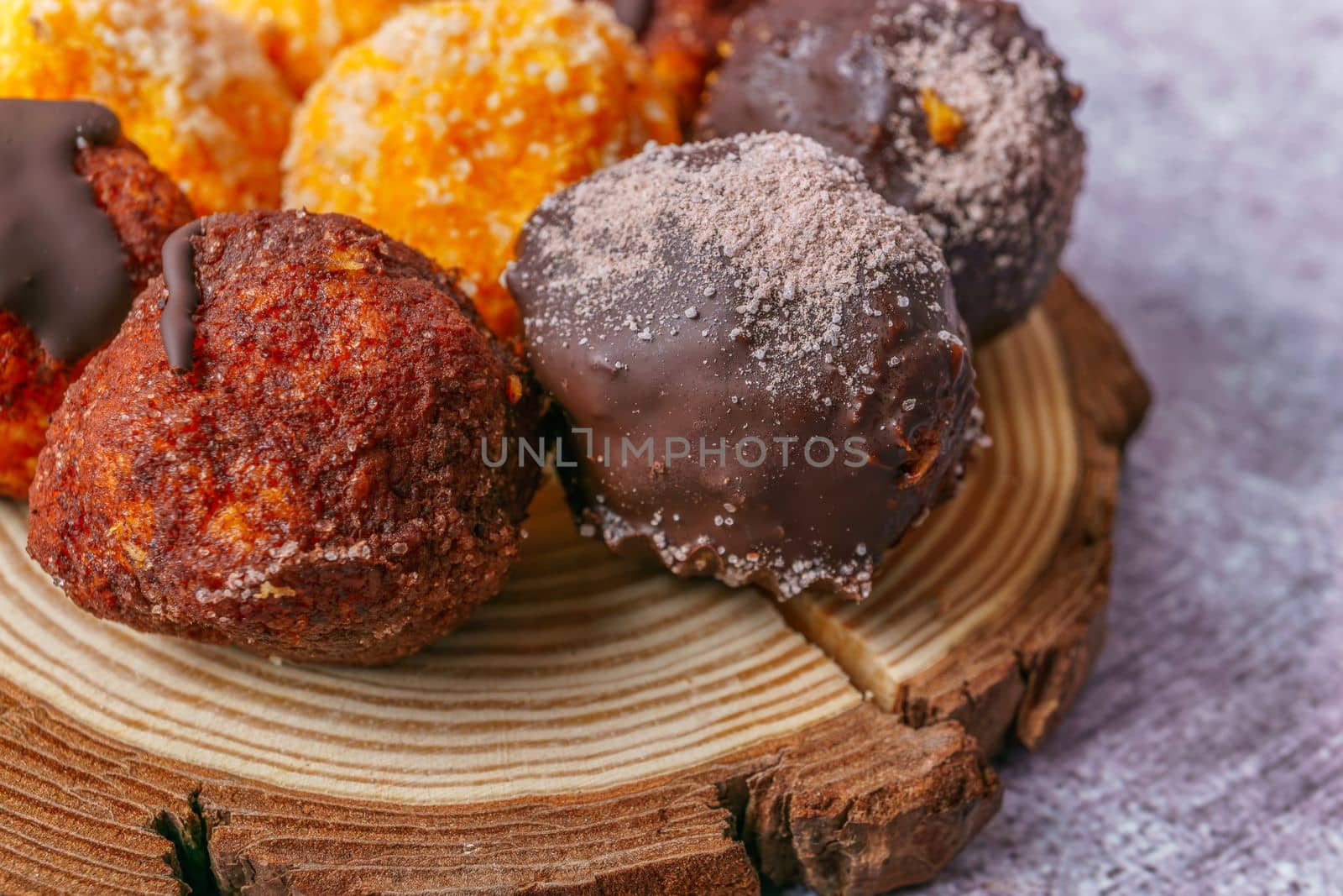 close-up of sweet truffles of different flavors on a wooden disk on a gray background