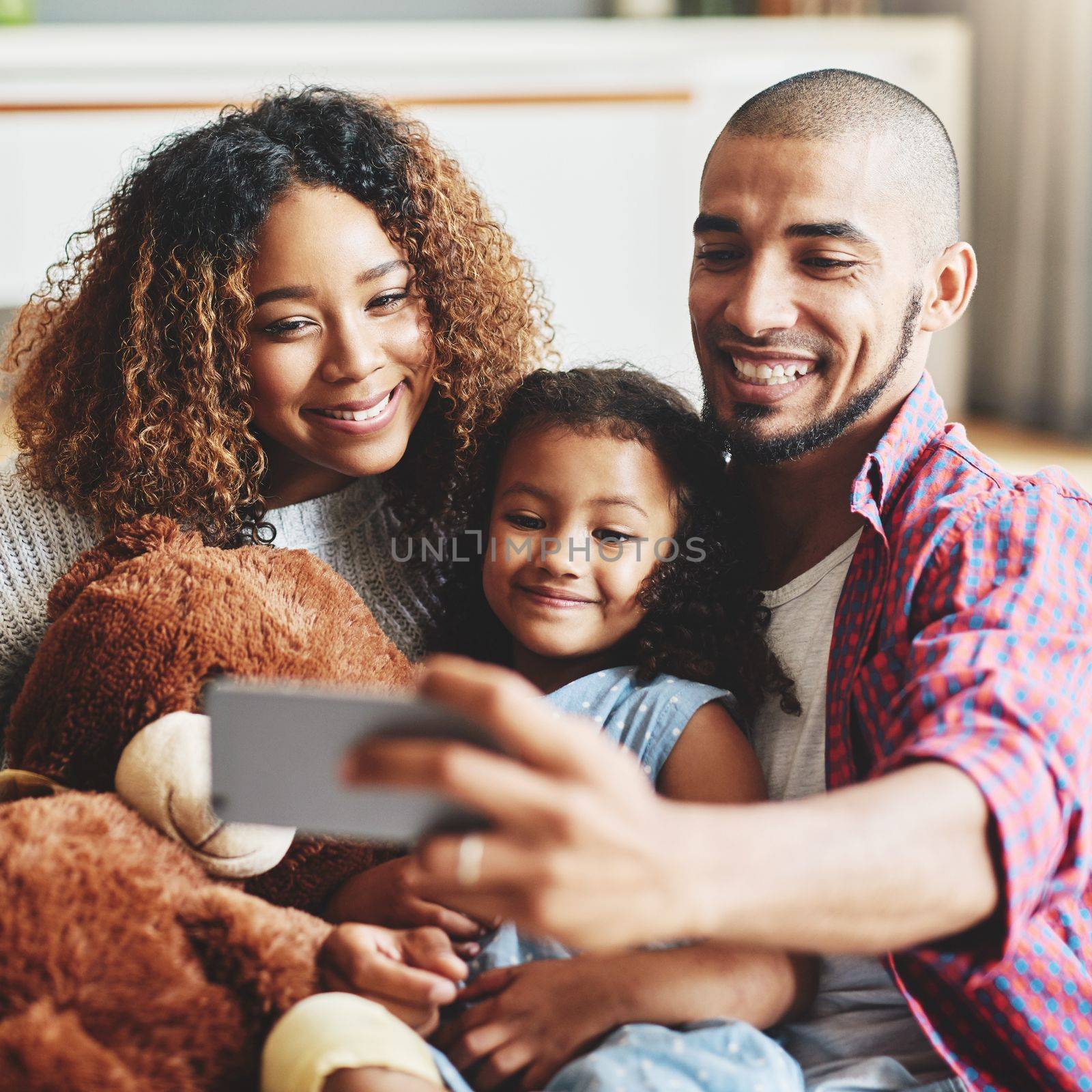 Arent they just perfect. a happy young family of three taking selfies together in their living room at home. by YuriArcurs