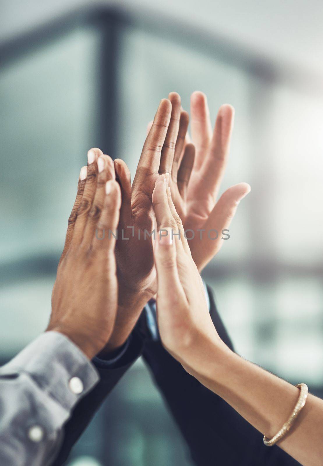 We did it together. a group of unrecognizable businesspeople high fiving in the office. by YuriArcurs