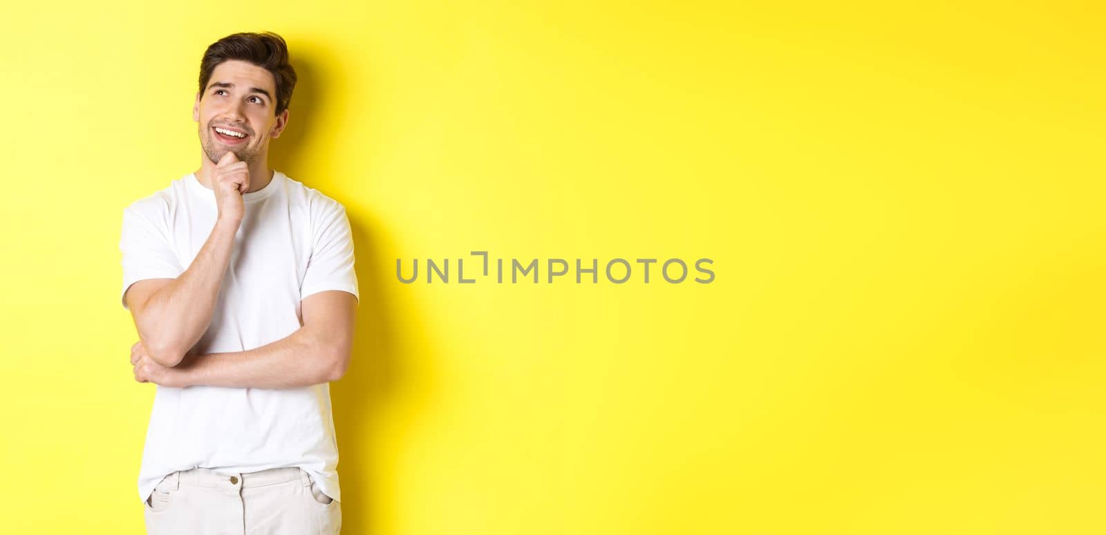 Portrait of smiling man looking thoughtful at upper left corner, choosing something, have an idea, standing against yellow background.