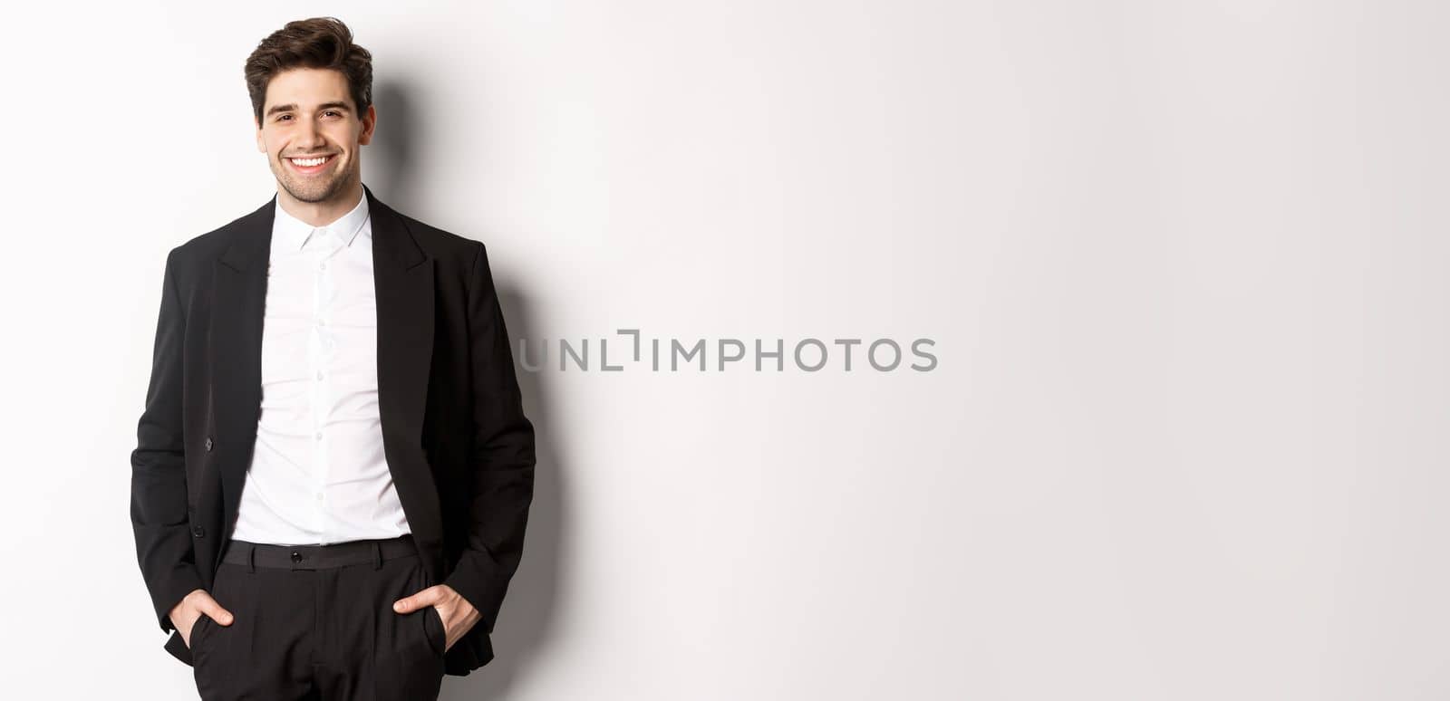 Image of handsome caucasian man in party suit, smiling pleased, attend formal event, standing over white background by Benzoix