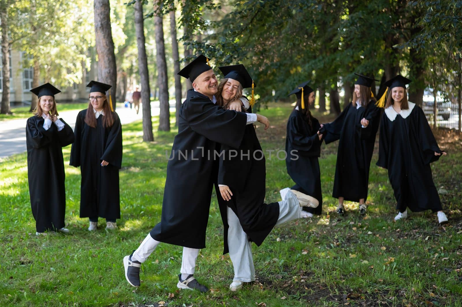 A group of graduates in robes congratulate each other on their graduation outdoors. by mrwed54