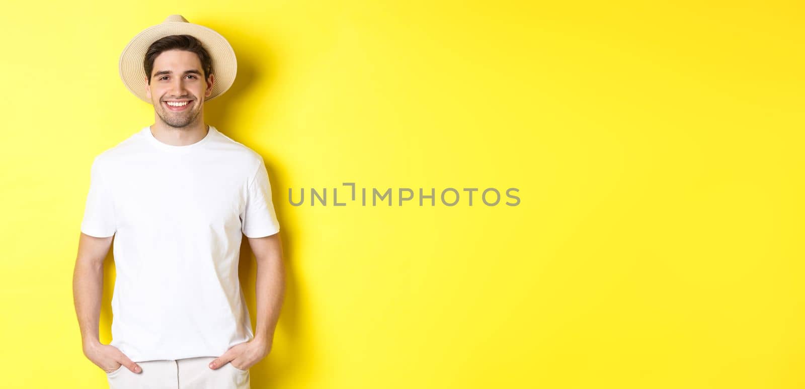 Young handsome guy tourist looking happy, wearing straw hat for travelling, standing against yellow background by Benzoix