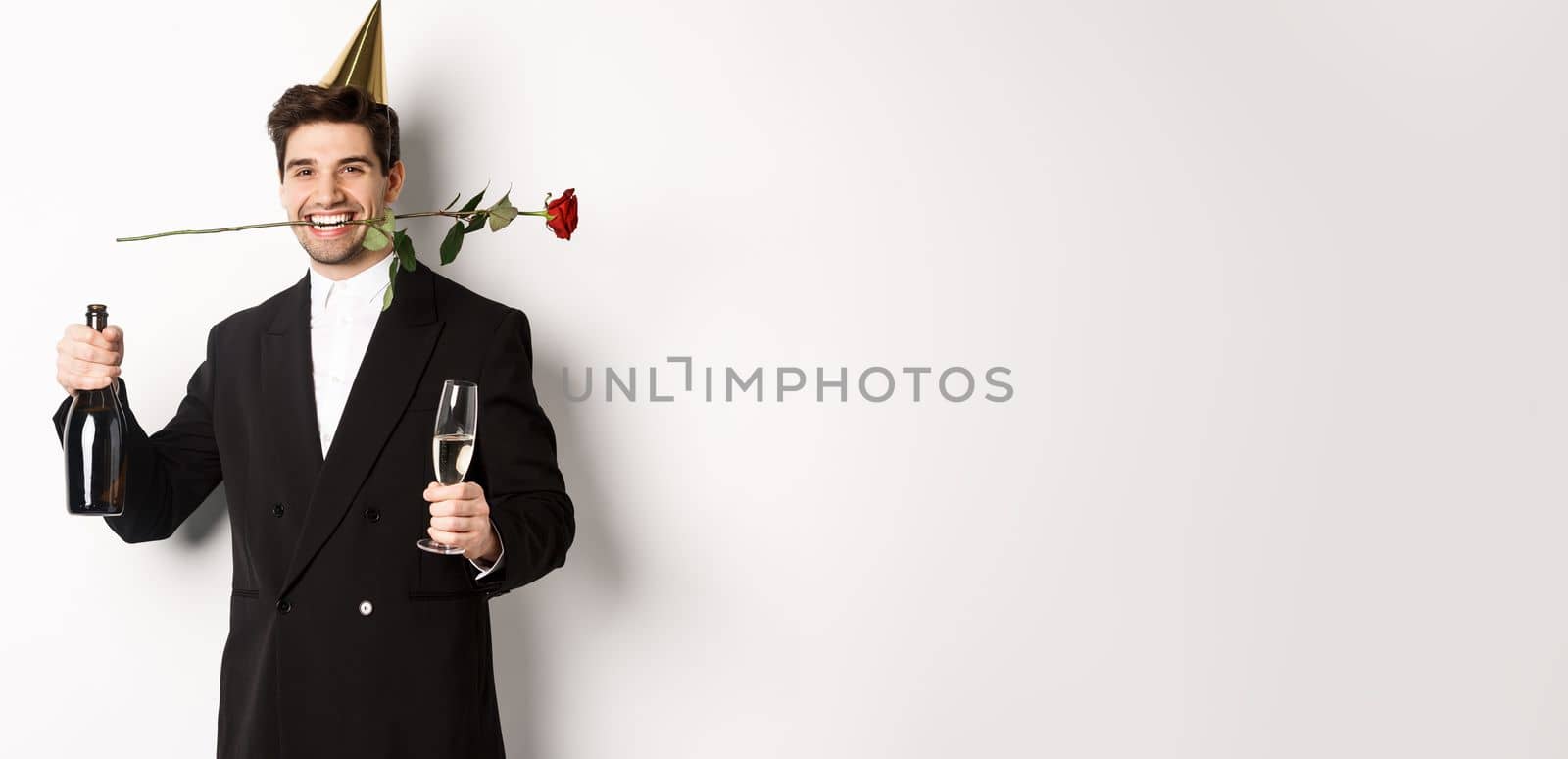 Funny guy in trendy suit, celebrating and having a party, holding rose in teeth and champagne, standing over white background by Benzoix