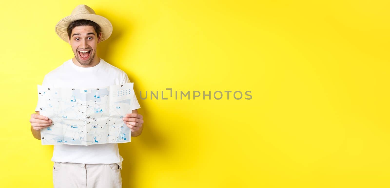 Travelling, vacation and tourism concept. Man tourist looking happy at map with sighsteeings, explore city, standing over yellow background.