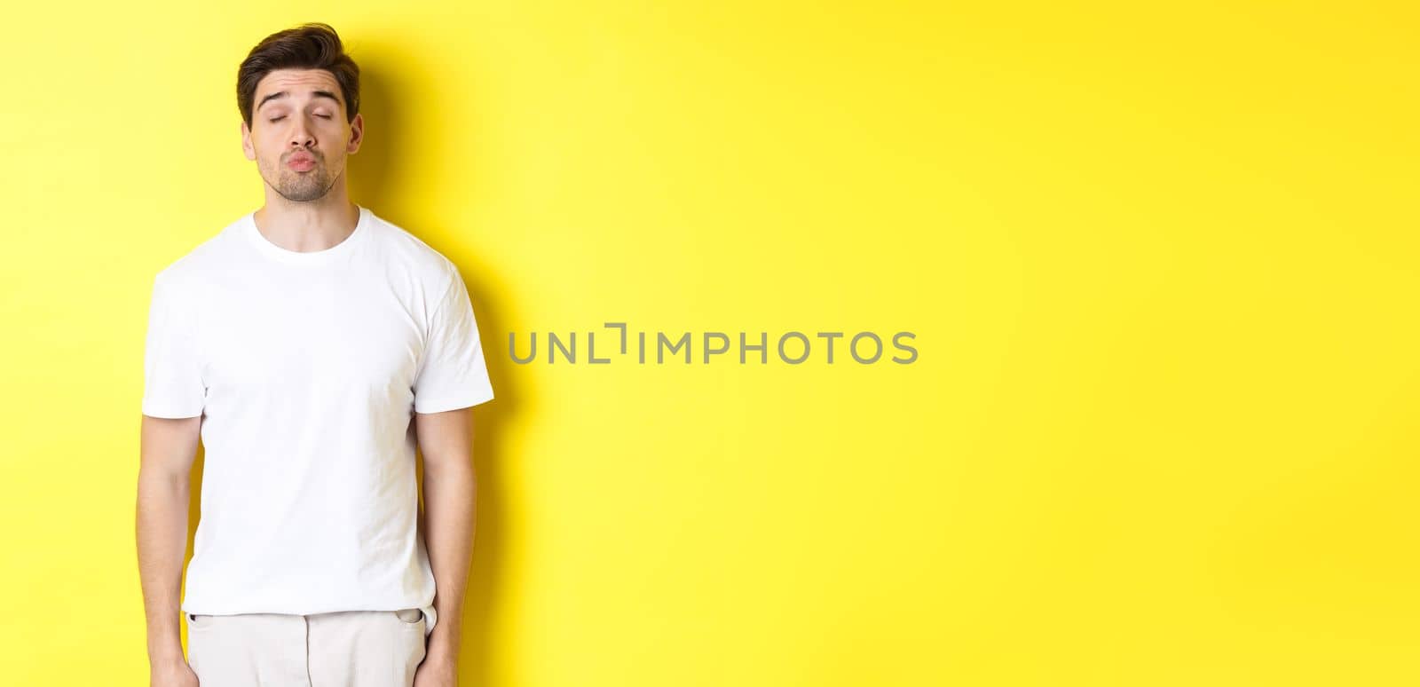 Image of lovely man close eyes and pucker lips, waiting for kiss, standing in white clothes against yellow background by Benzoix